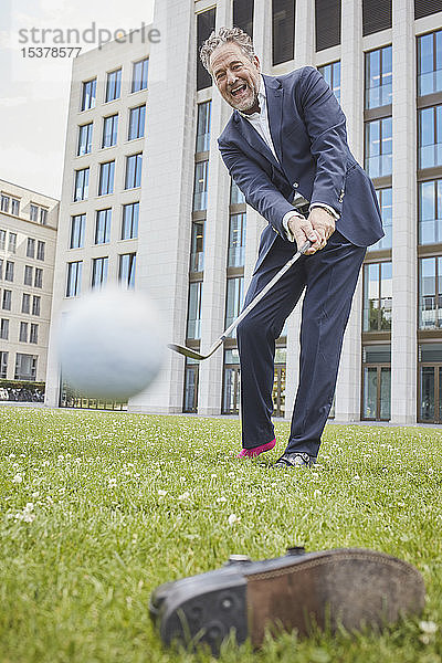 Glücklicher reifer Geschäftsmann spielt Golf auf dem Rasen in der Stadt