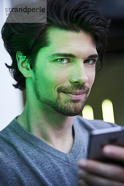 Nahaufnahme eines selbstbewussten Mannes mit grünem Licht  der ein Mobiltelefon hält