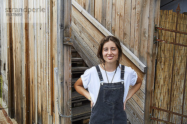 Porträt einer lächelnden jungen Frau vor einem Holzzaun