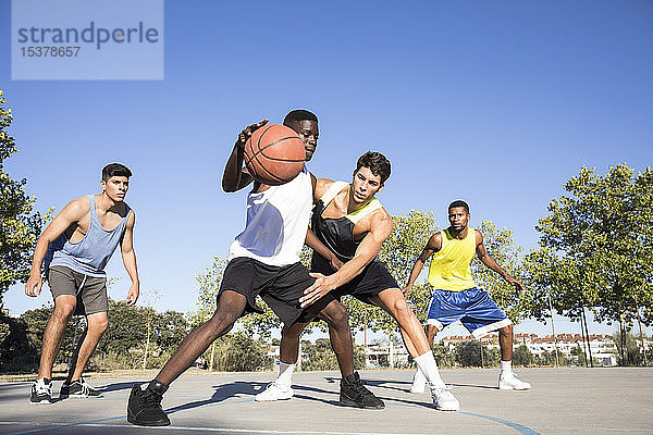 Junge Männer spielen Basketball und dribbeln Ball auf dem Sportplatz