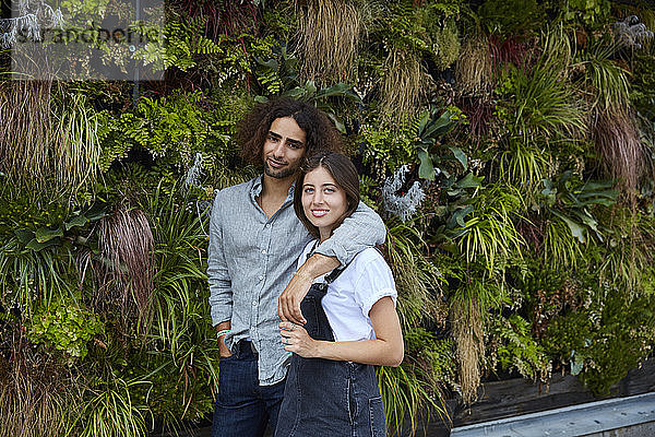 Porträt eines lächelnden jungen Paares vor einer Pflanzenwand