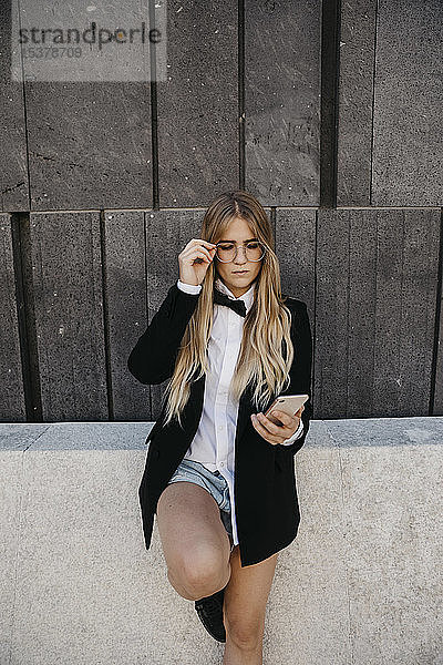 Porträt einer blonden jungen Frau mit schwarzer Krawatte und Blazer  die auf ihr Handy schaut  Wien  Österreich