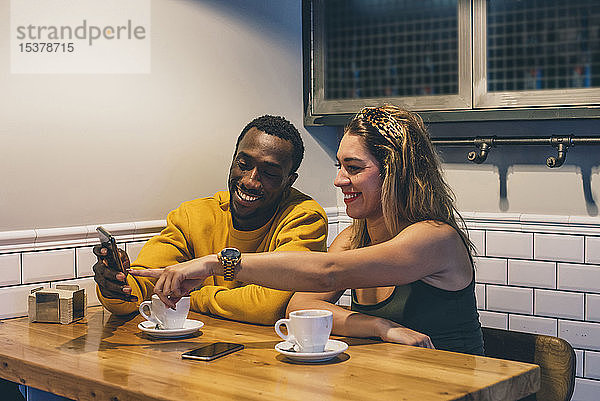 Porträt eines lächelnden Paares in einem Café mit Smartphone