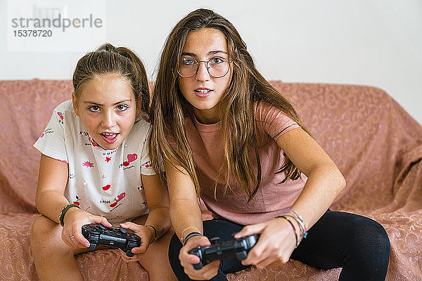 Schwestern spielen zu Hause auf der Couch Videospiele