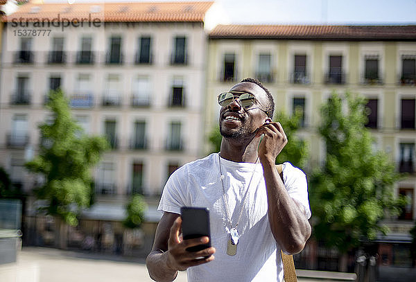 Lächelnder junger Mann benutzt Smartphone und Kopfhörer und schaut auf