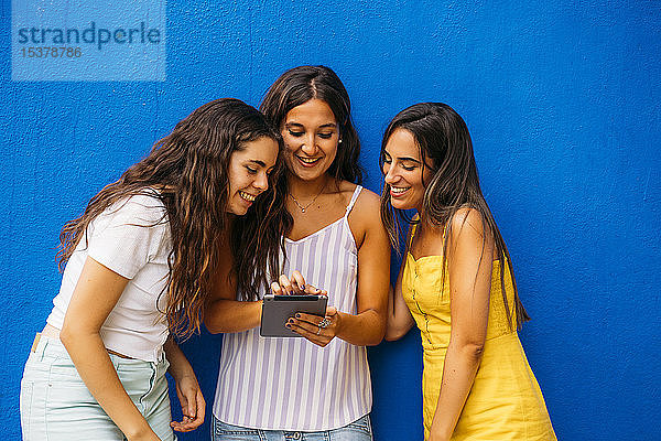 Drei glückliche Freundinnen stehen an einer blauen Wand und teilen sich ein Tablett