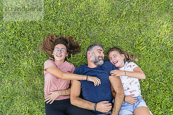 Glücklicher Vater mit zwei Töchtern auf einer Wiese liegend