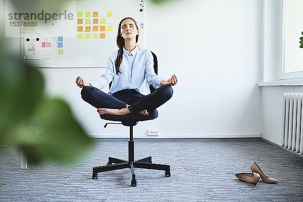 Gelassene junge Frau meditiert  während sie auf einem Bürostuhl sitzt