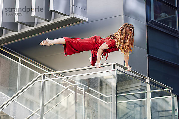 Sportliche junge Frau macht Akrobatik auf einem Geländer