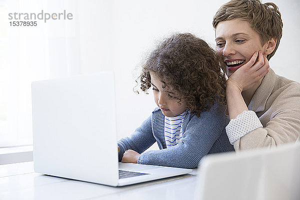 Lächelnde Mutter und Sohn benutzen Laptop zu Hause