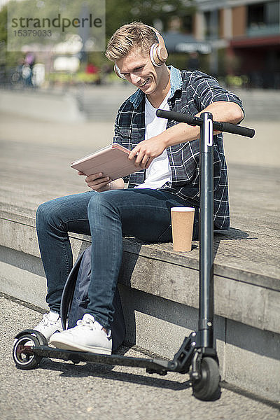 Junger Mann mit E-Scooter mit Tablette in der Stadt