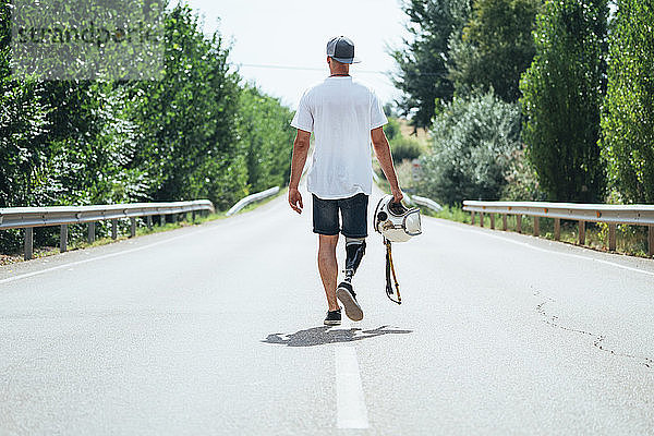 Junger Mann mit Beinprothese  der mit einem Helm die Straße entlang geht