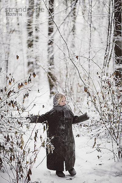 Kleines Mädchen im Mantel im Winterwald stehend