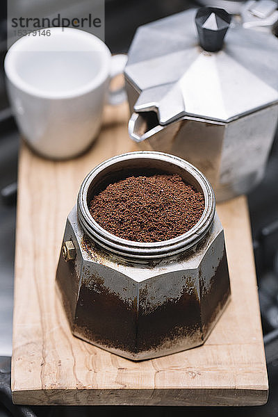 Hochwinkelansicht von gemahlenem Kaffee mit Behälter mit Tasse und Kaffeemaschine auf Holztablett in der Küche
