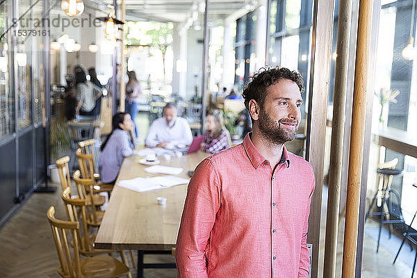 Porträt eines Gelegenheits-Geschäftsmannes in einem Cafe mit Kollegen  die im Hintergrund ein Treffen haben