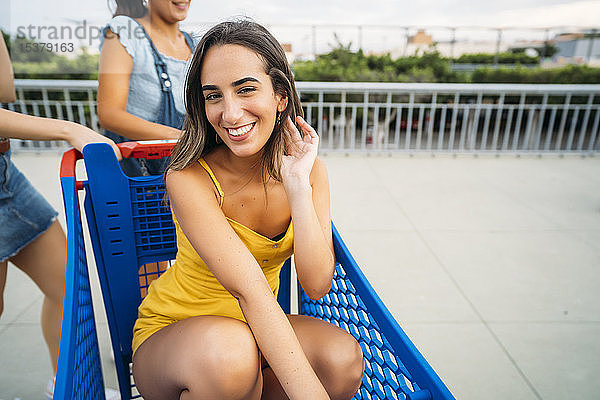 Porträt einer lächelnden jungen Frau mit Freunden in einem Einkaufswagen