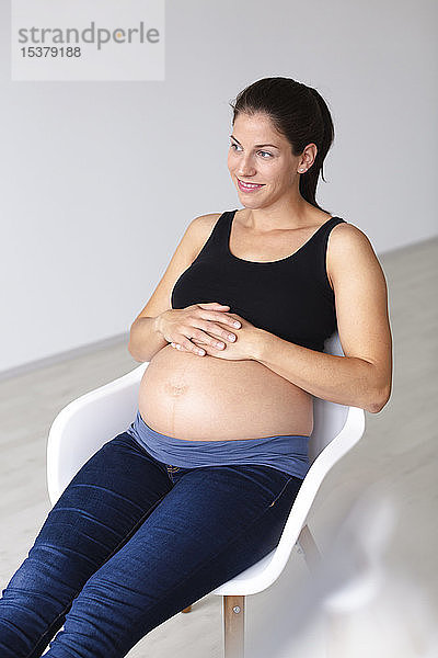 Junge schwangere Frau sitzt auf einem Stuhl und denkt über die Zukunft nach