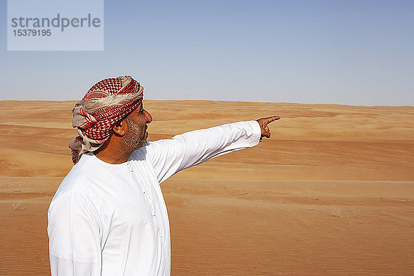 Beduine in Nationaltracht in der Wüste stehend  auf Distanz zeigend  Wahiba Sands  Oman