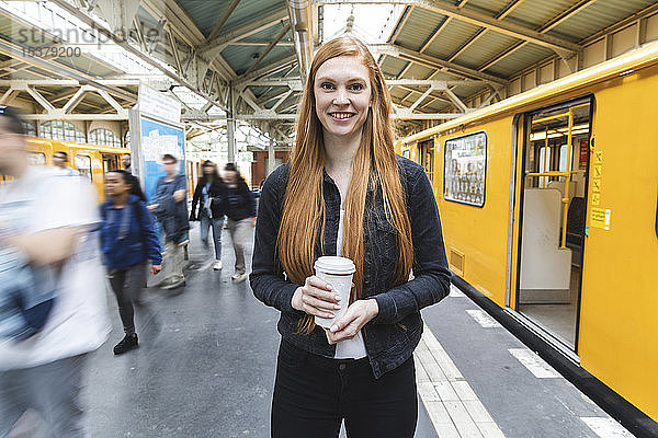 Porträt einer rothaarigen jungen Frau mit Kaffee auf dem Bahnsteig  Berlin  Deutschland