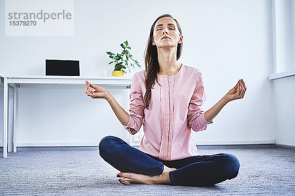 Junge Frau meditiert im Büro auf dem Boden