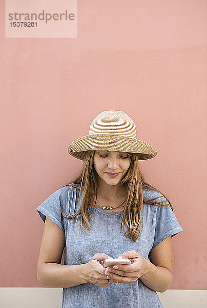 Frau steht mit einem Smartphone an einer rosa Wand