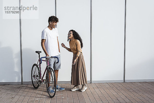 Glückliches Paar mit Fahrrad vor weißem Zaun stehend  lachend