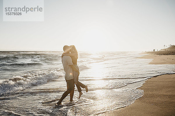 Liebenswertes junges Paar umarmt sich bei Sonnenuntergang am Meeresufer