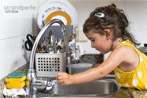 Kleines Mädchen spült zu Hause Geschirr aus dem Wasserhahn in der Küche