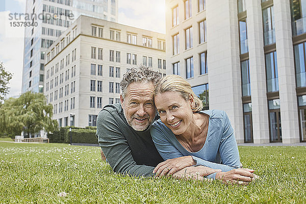Porträt eines glücklichen  reifen Paares  das auf dem Rasen in der Stadt liegt
