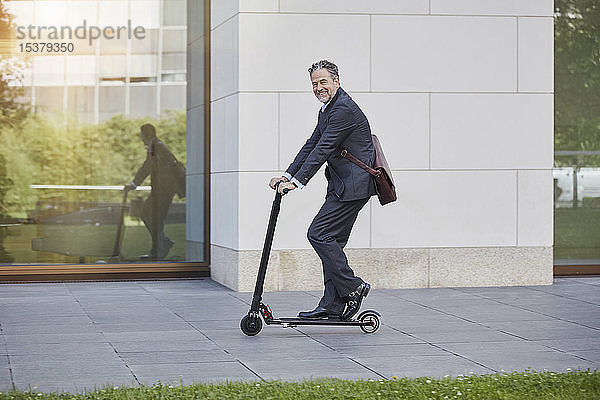 Geschäftsmann auf E-Scooter fährt an Bürogebäude in der Stadt vorbei