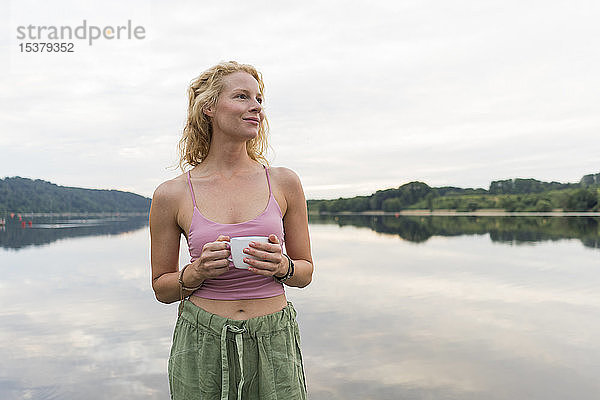Junge Frau trinkt Kaffee aus Tasse an einem See