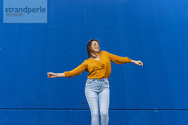 Junge tanzende Frau vor einer blauen Wand
