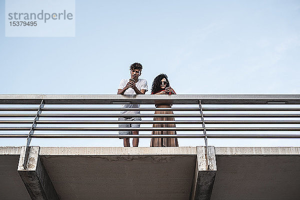 Junges Paar steht auf der Brücke und benutzt Smartphones