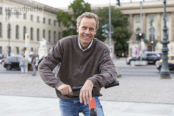 Porträt eines glücklichen älteren Mannes  der sich auf einen Elektroroller stützt  in der Stadt  Berlin  Deutschland