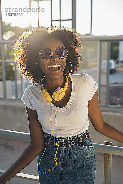 Porträt einer lachenden jungen Frau mit Sonnenbrille und Kopfhörer