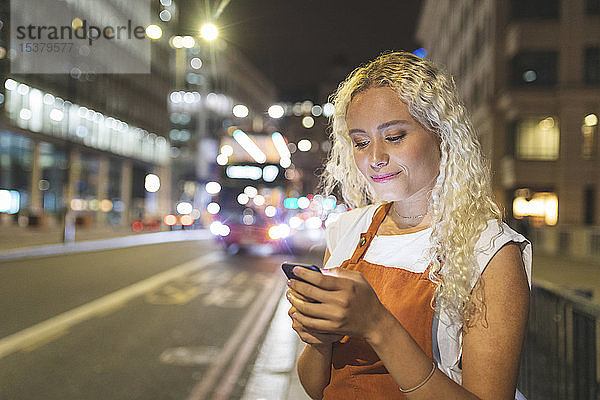 Junge Frau in London schaut nachts auf ihr Smartphone