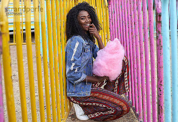 Porträt einer glücklichen jungen Frau mit rosa Zuckerwatte auf dem Jahrmarkt