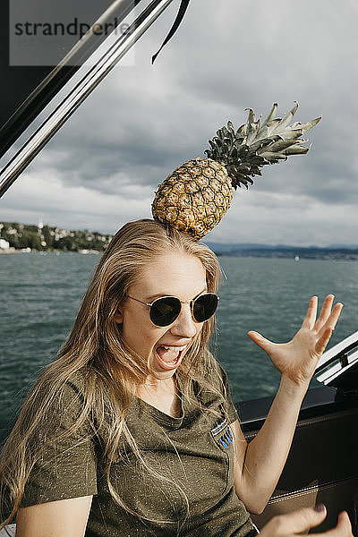 Schreiende junge Frau auf einem Boot  die eine Ananas auf ihrem Kopf balanciert