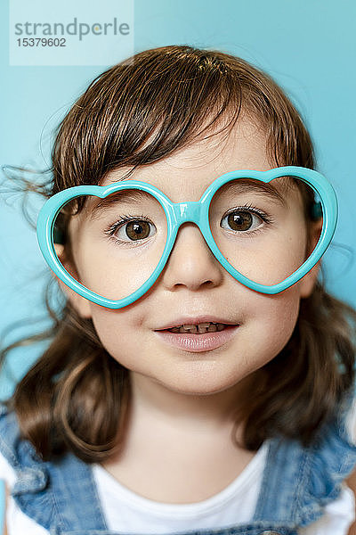 Bildnis eines süßen kleinen Mädchens mit herzförmiger Brille auf blauem Hintergrund