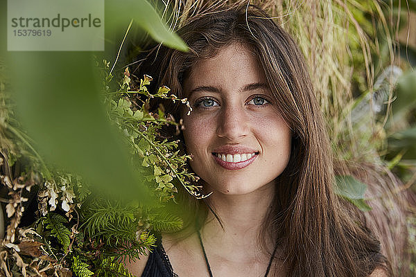 Porträt einer lächelnden jungen Frau vor einer Pflanzenwand