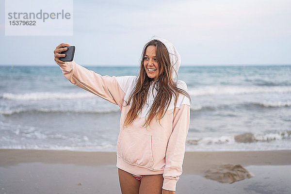 Glückliche junge Frau  die am Strand ein Selfie macht