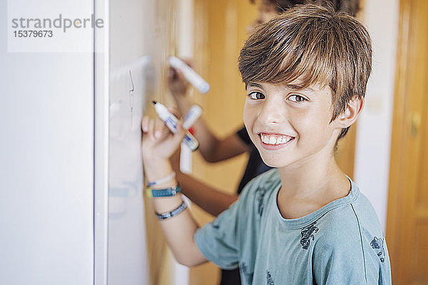 Porträt eines lächelnden Jungen mit einem Freund  der auf einer Tafel zeichnet