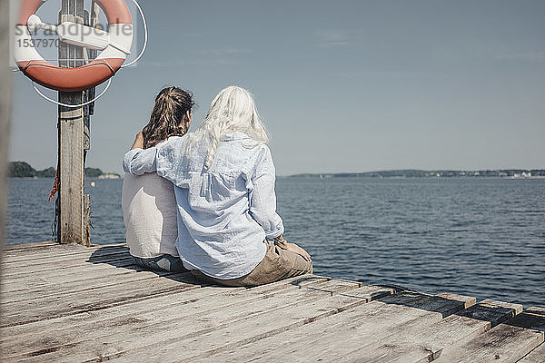 Mutter und Tochter schauen auf das Meer  auf dem Steg sitzend  Rückansicht