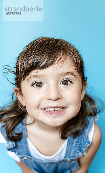 Porträt eines niedlichen kleinen Mädchens  das sehr ausdrucksstark lächelt  auf blauem Hintergrund