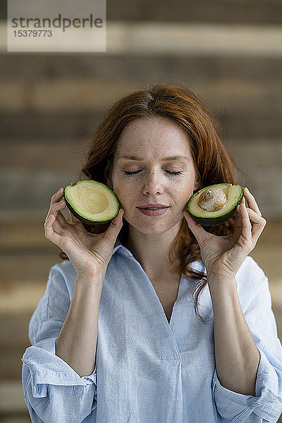Porträt einer rothaarigen Frau mit geschlossenen Augen  die eine in Scheiben geschnittene Avocado hält
