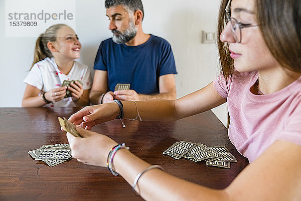 Vater mit zwei Töchtern spielt zu Hause Karten auf einem Holztisch
