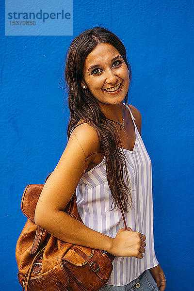 Porträt einer schönen jungen Frau mit Rucksack an einer blauen Wand