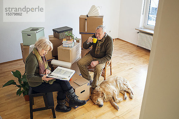 Älteres Ehepaar macht eine Pause  umgeben von Pappkartons in einem leeren Raum