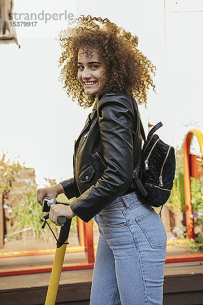 Porträt einer lächelnden Teenagerin mit Rucksack und Roller