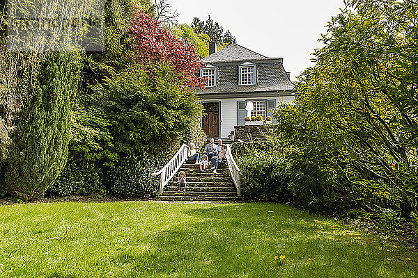 Großfamilie  die auf einer Treppe im Garten ihres Hauses sitzt